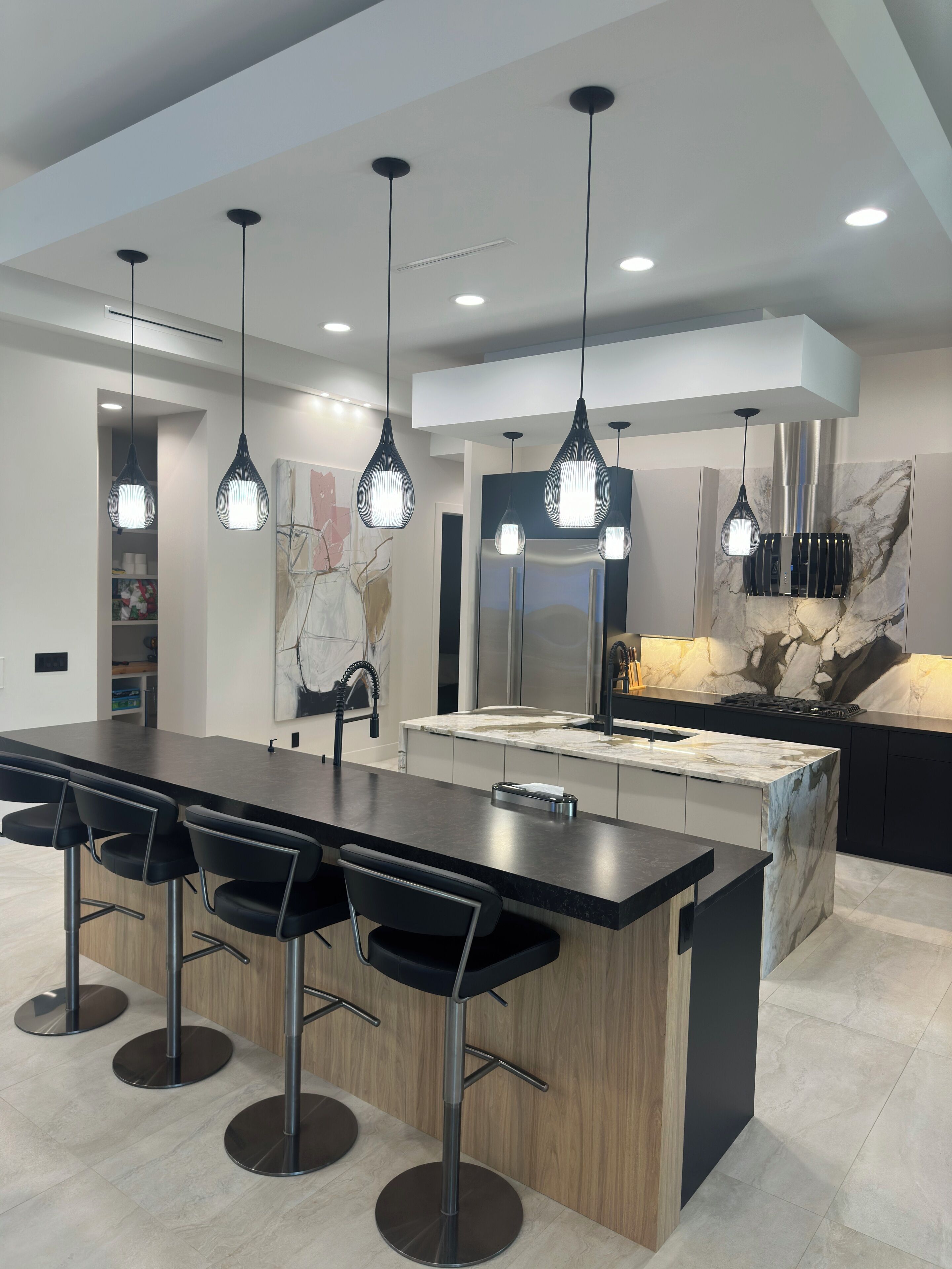 A modern kitchen with a central island, bar stools, pendant lighting, and a marble backsplash.