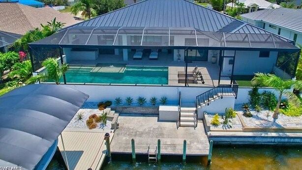 Ein modernes Haus mit einem großen Schwimmbecken, einer überdachten Terrasse und einem Steg, der ins Wasser führt.