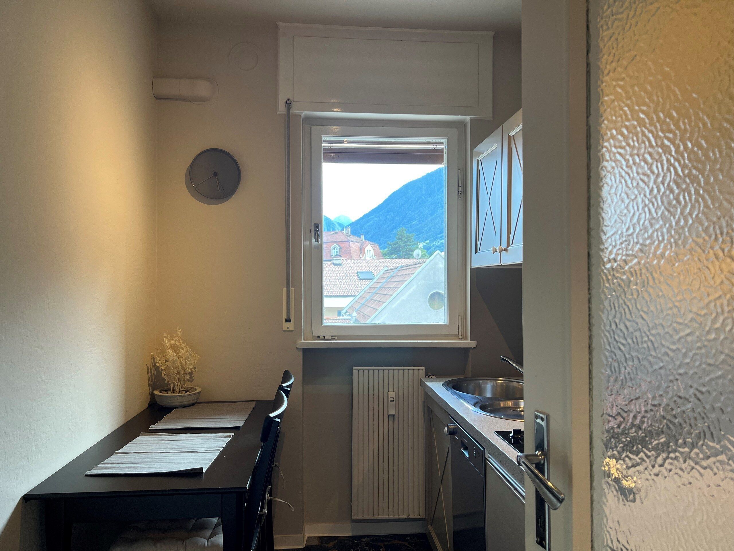 A compact kitchen with a window, a radiator, and a small dining area.