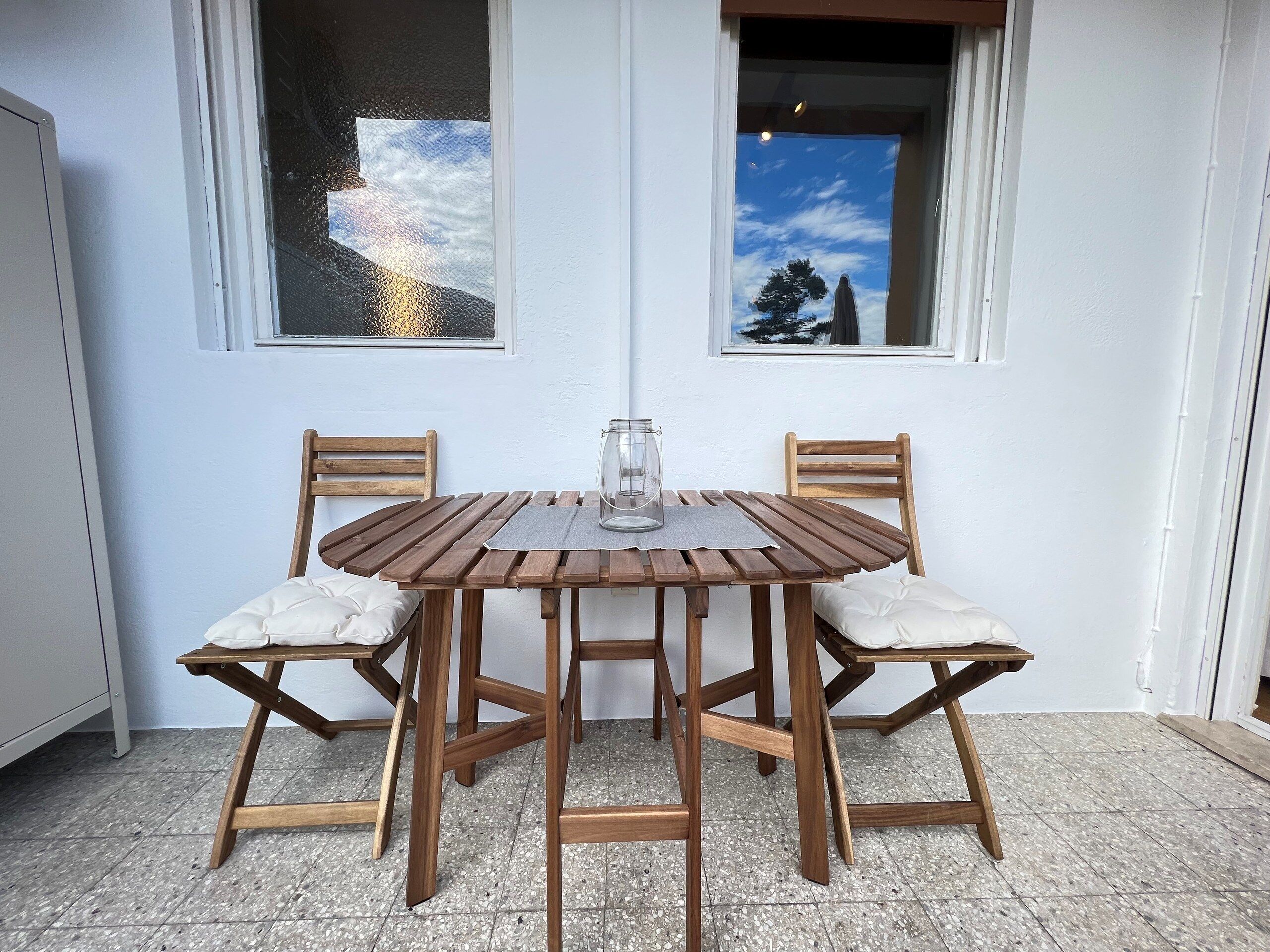 Una mesa redonda de madera con cuatro sillas, una jarrón de vidrio y un cojín blanco en cada silla.