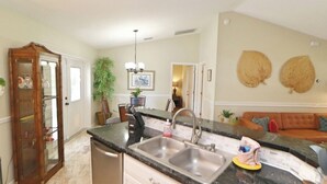 A kitchen with a double sink, a wooden cabinet, and a dining area with a sofa. - Your Palm Coast Pool House! (Palm Coast)