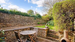 A stone wall with a garden, a wooden table and chairs, and a rustic chimney. - Mouse Manor - pet friendly, Longborough near Stow-on-the-Wold (Longborough)