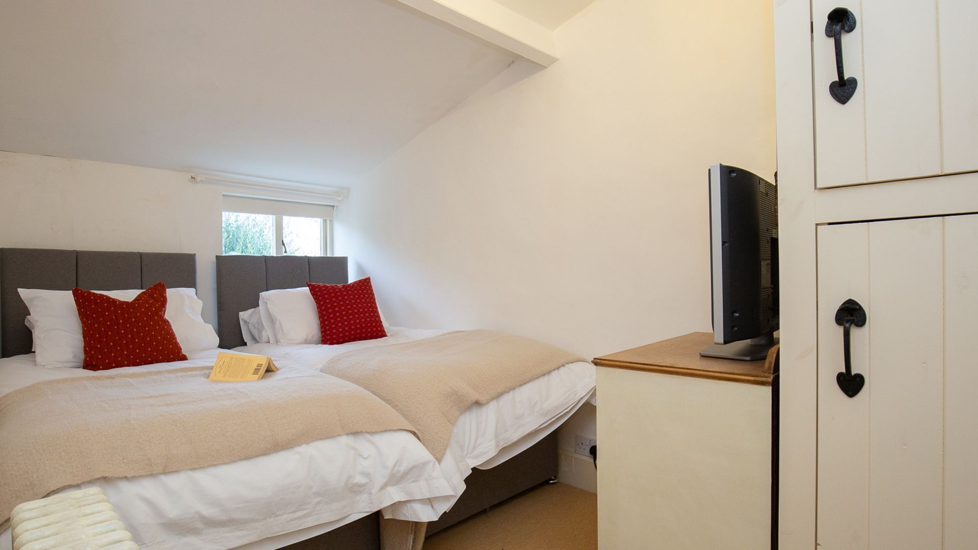 A bedroom with two beds, a television on a stand, and a wardrobe with a heart-shaped handle.