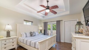 A bedroom with a bed, nightstands, a ceiling fan, a window, and a door leading to an outdoor area. - Ocean Breeze Getaway  (Deerfield Beach)