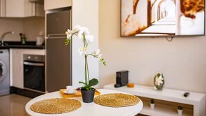 A modern kitchen with white cabinets, a refrigerator, and a dining area with a round table and two woven placemats. - Studio in the heart of Casablanca (Casablanca)