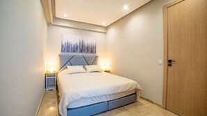 A bedroom with a bed, bedside tables, a wall-mounted artwork, a wooden door, and a carpeted floor. - Studio in the heart of Casablanca (Casablanca)
