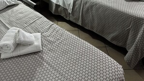 Habitación de hotel con dos camas, una mesita de noche con lámpara, un armario y toallas dobladas con cuidado.
