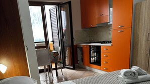 Habitación de hotel con cama, kitchenette pequeña y puerta corredera que da a un balcón.