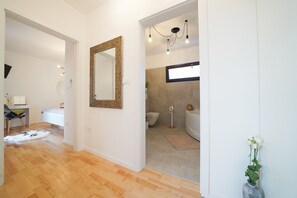 A modern interior with a wooden floor, a large mirror, a desk with a chair, and a bathroom with a bathtub and toilet. - Villa Fusion with Pool (Sukošan)