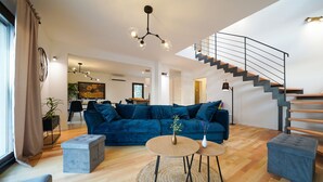A modern living room with a blue sofa, a round coffee table, and a staircase. - Villa Fusion with Pool (Sukošan)