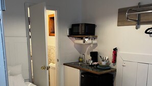 Een compacte kamer met een bed, een kitchenette, een kleine koelkast en een witte prullenbak.