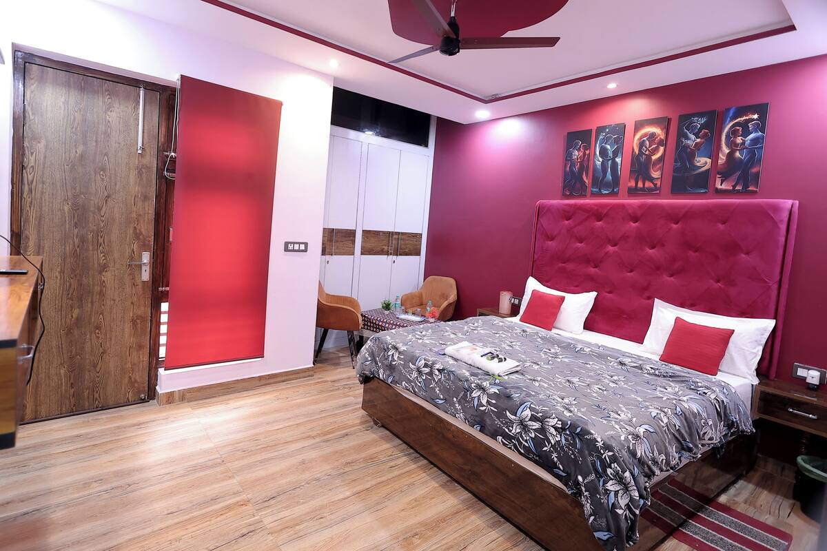 Une chambre avec un grand lit, un ventilateur de plafond, une armoire en bois et un mur d’accent rouge.