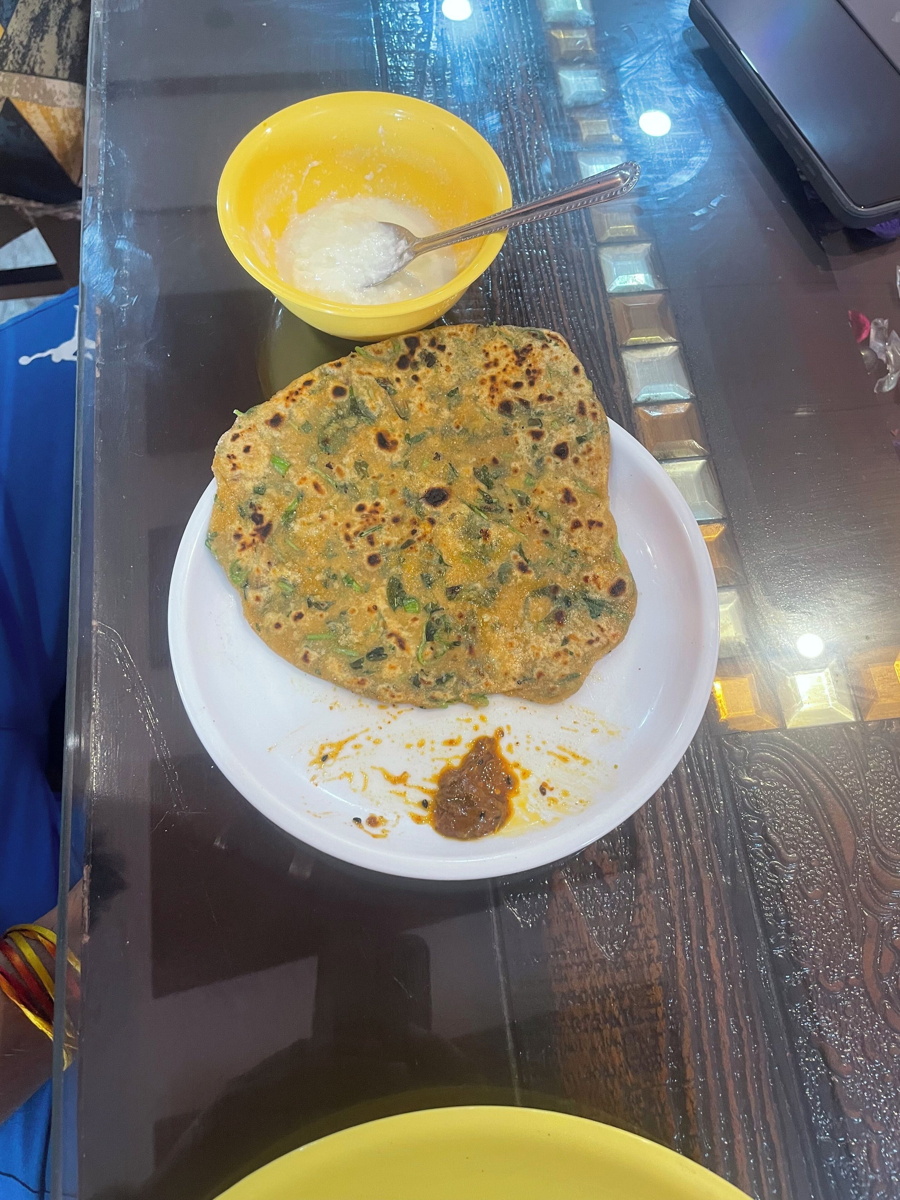 A plate with a piece of food and a yellow bowl with a spoon on a table.