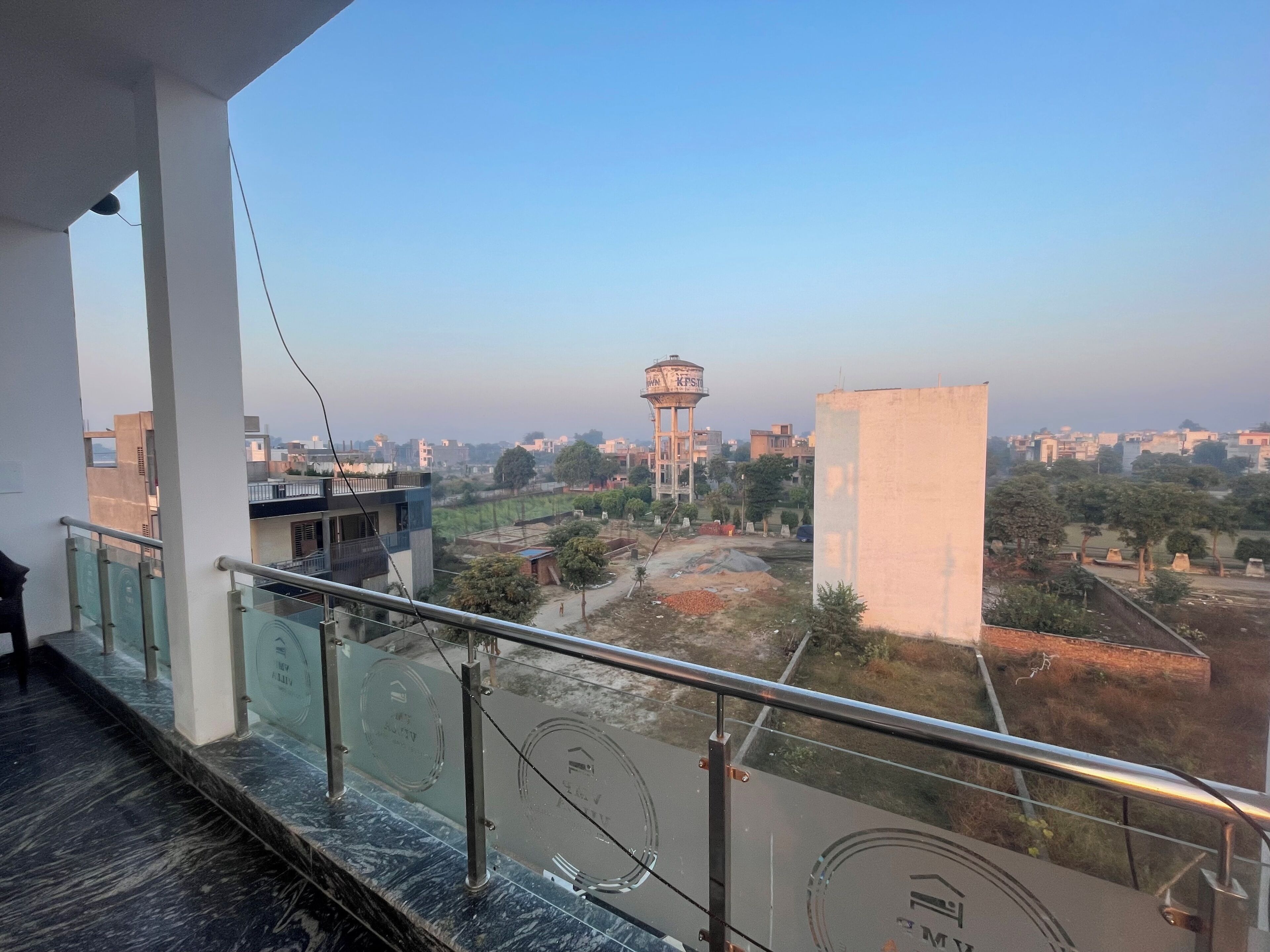 A balcony with a metal railing overlooking a residential area with houses, trees, and a water tower.