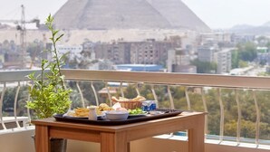A balcony with a tray of food, a potted plant, and a view of the pyramids in the background.