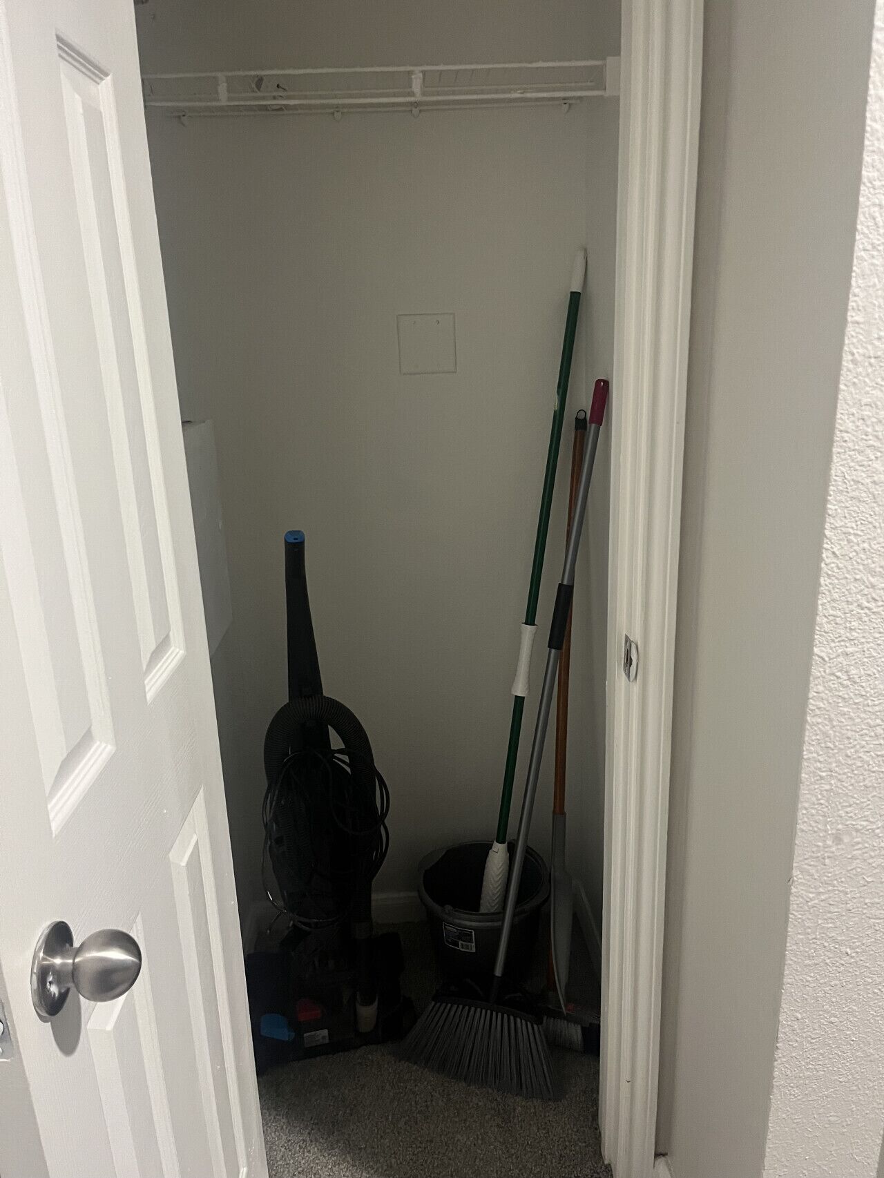Ein enger Korridor mit einer geschlossenen Tür links, einem an die Wand gelehnten Besen und einem Mülleimer in der Mitte.