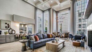 Un vaste salon comprenant un grand canapé, une table basse et un coin salon. Au fond, on trouve une cuisine équipée d’appareils électroménagers modernes, ainsi qu’un coin repas avec des chaises.