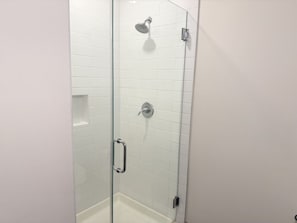 A glass-enclosed shower stall with white tiled walls, a handheld showerhead, and a wall-mounted faucet.
