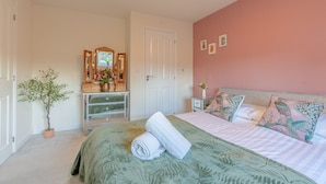 Un dormitorio con cama, cómoda, espejo, planta en maceta y una puerta.