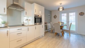 Una cocina moderna con armarios blancos, una campana extractora de acero inoxidable y un comedor con mesa y sillas.