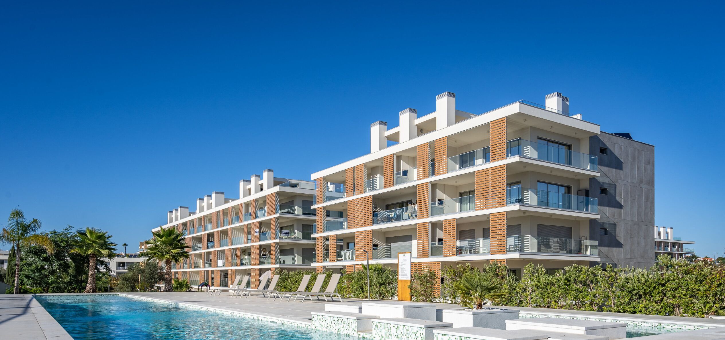 Un hôtel moderne à plusieurs étages, doté d’une piscine, de balcons et offrant une vue sur un ciel d’un bleu éclatant.