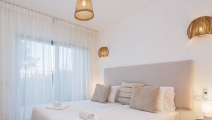 Une chambre à coucher avec un grand lit, des rideaux blancs et deux lampes fixées au mur.