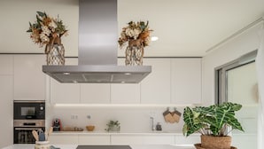 Une cuisine moderne avec des meubles blancs, une hotte de cuisinière en acier inoxydable et des vases décoratifs suspendus au plafond.