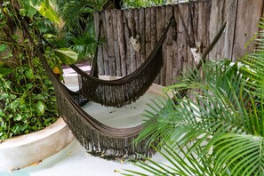 Relax in a hammock suspended between two posts, surrounded by lush greenery and tropical plants.