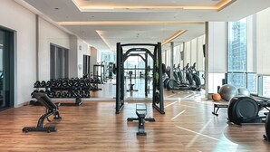 A modern gym with various exercise equipment, large windows, and a spacious layout. - New Cosy 1BR with Pool & Gym in City Centre (Dubai)