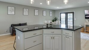 Una cocina moderna con una isla central, armarios blancos e iluminación colgante.