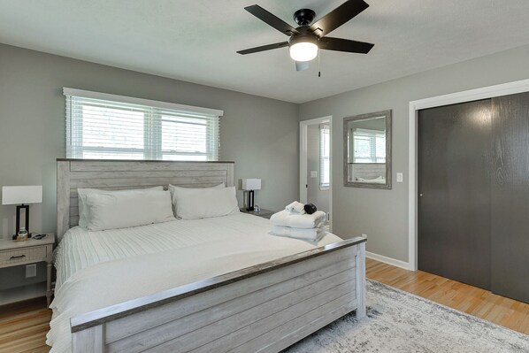 A bedroom with a bed, bedside lamps, a ceiling fan, a dark door, and a window with blinds.