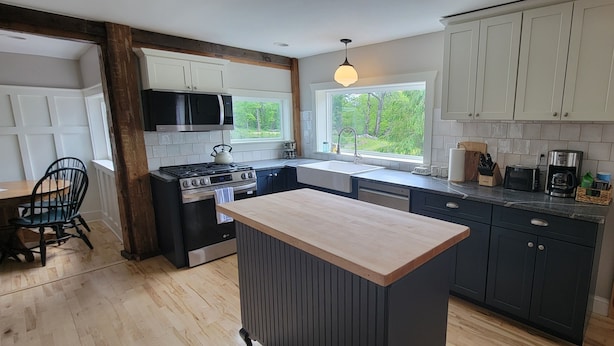 A modern kitchen with dark cabinets, a wooden island, a built-in microwave, and a window offering a view of greenery.