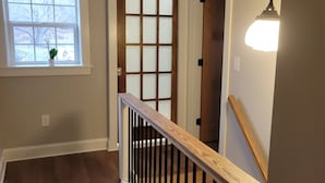 A wooden staircase with a white handrail and black balusters, leading to a room with a wooden door and a window with frosted glass panes.