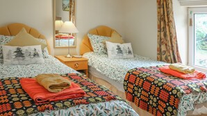 Ein Schlafzimmer mit zwei Betten, jeweils mit gemusterten Bettwäsche und Kissen, einem Nachttisch mit Lampe sowie einem Fenster mit Vorhängen.
