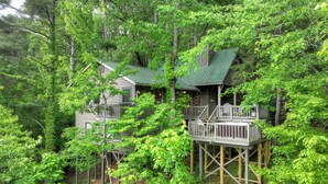 A cabin with a green roof and wooden deck, surrounded by dense forest. - Cabin in Blue Ridge: Hot Tub|Fire Pit|Fooseball (Cherry Log)
