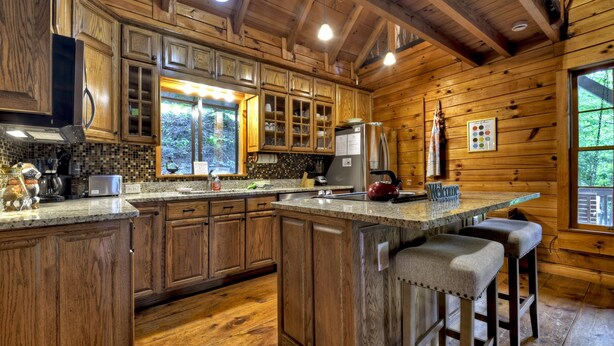 A wooden cabin-style kitchen with a large island, wooden cabinets, and a view of the outdoors. - Cabin in Blue Ridge: Hot Tub|Fire Pit|Fooseball (Cherry Log)