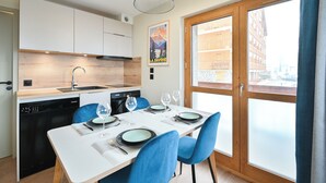 Una cocina moderna con armarios blancos, lavavajillas y una zona de comedor con una mesa para dos.