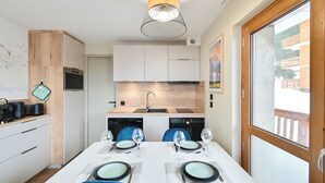 Una cocina moderna con armarios blancos, encimera de madera y zona de comedor con una mesa blanca preparada para cuatro.