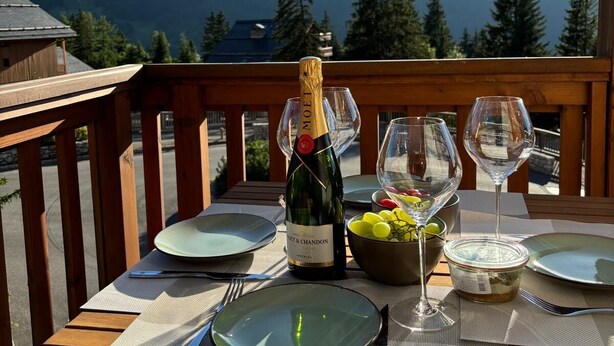 Una terraza de madera con una mesa preparada para una comida, una botella de vino y un bol de uvas.