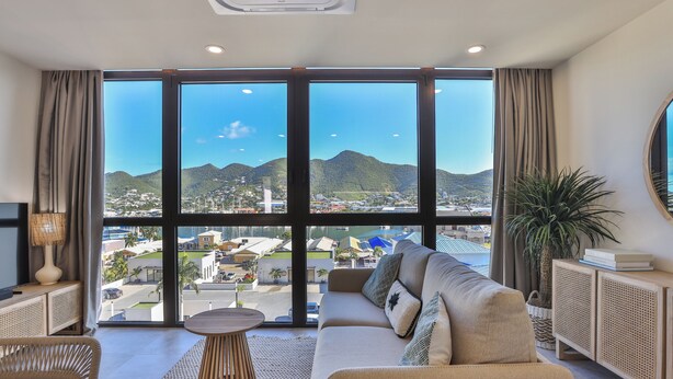 A modern living room with a large window, a sofa, a round coffee table, and a television.