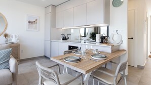 A modern kitchen with white cabinets, a wooden dining table set for four, and a large mirror above the counter.