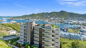 A modern multi-story building with a rooftop garden, surrounded by lush greenery and a marina with boats.