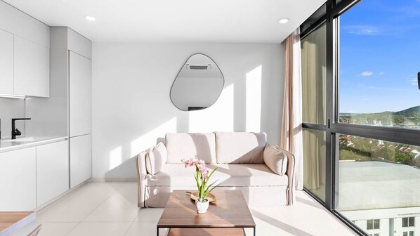 A modern living room with a sofa, a coffee table with a plant, and a view of a cityscape through large windows.