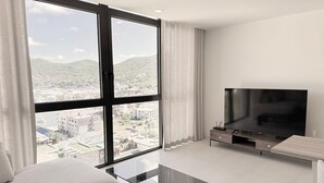 Una sala de estar moderna con un ventanal grande, un televisor de pantalla plana, una mesa de centro de vidrio y un sofá.