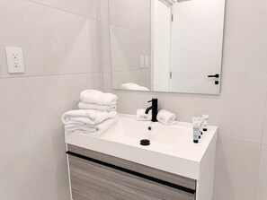 A modern bathroom with a white sink, black faucet, and a mirror above it. There are towels stacked on the sink and toiletries on the counter.