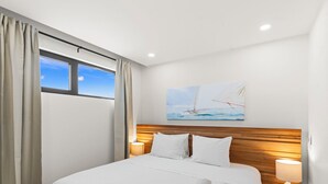 A modern hotel room with a large bed, wooden headboard, and a painting of a sailboat on the wall. - B237 - Cosy 1 Bedroom with Lagoon View (Sint Maarten)