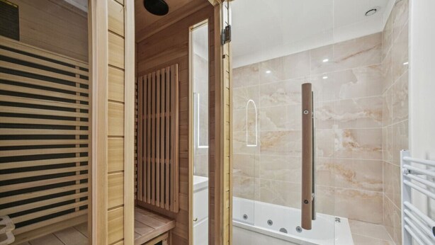 A modern bathroom with a glass-enclosed shower, a wooden vanity, and a marble-tiled wall.