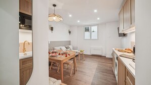 A modern kitchen with wooden cabinets, a dining area with a table set for two, and a window providing natural light.