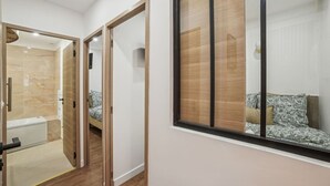 A modern interior with a wooden floor, a large window with a view of a bed, and a bathroom with a bathtub and toilet.