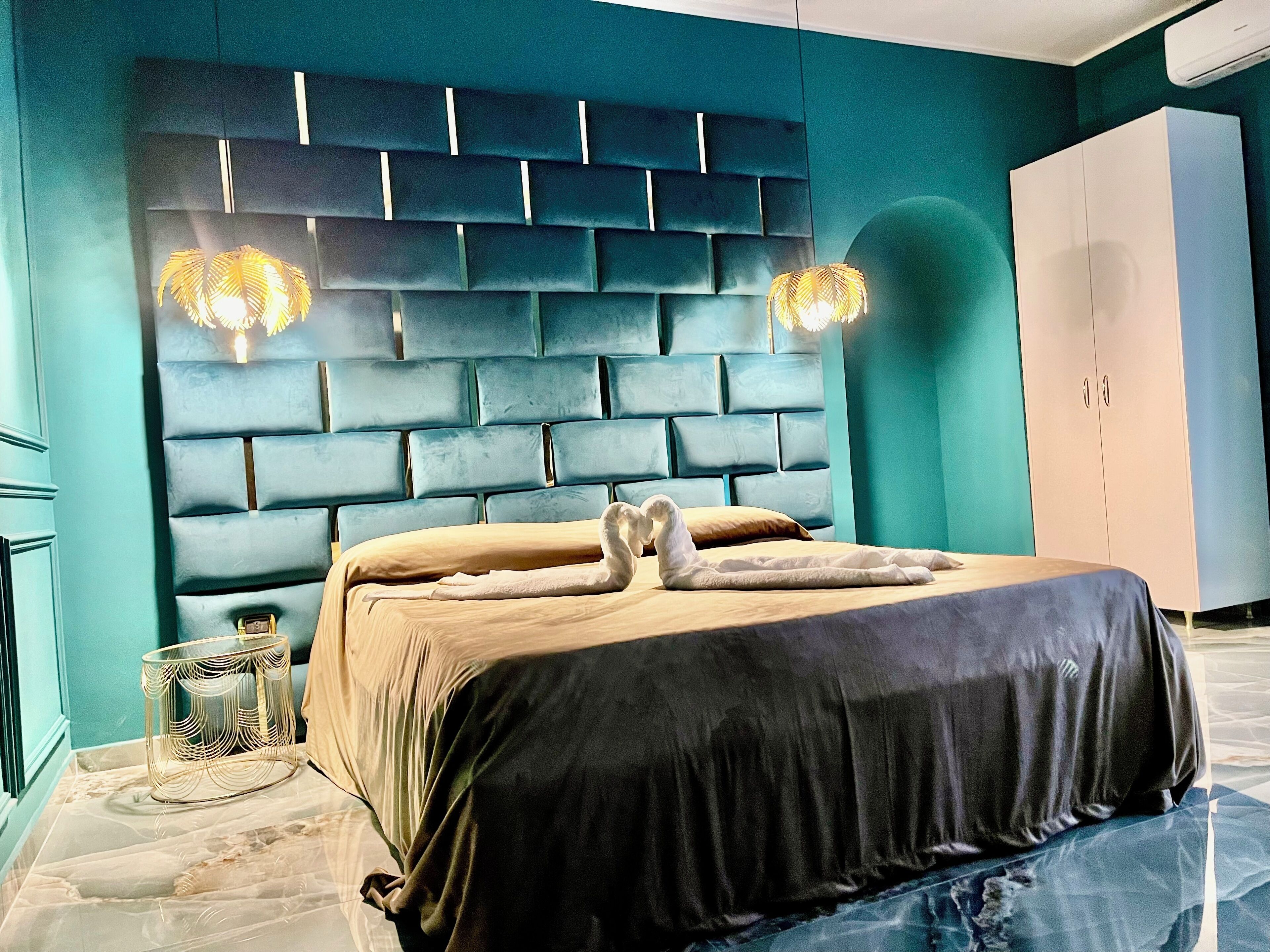 Une chambre à coucher moderne avec une tête de lit capitonnée, un lit recouvert d’une couverture foncée et une armoire blanche.